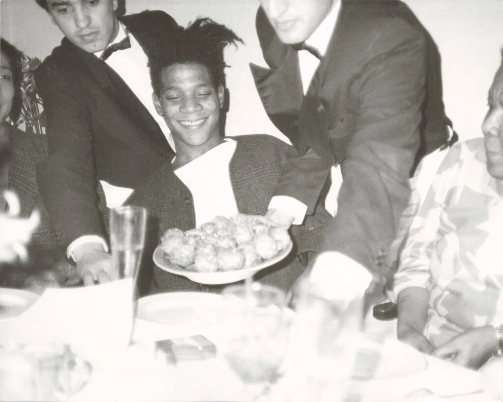 JEAN-MICHEL BASQUIAT DINNER AT MR. CHOW, 1985 UNIQUE GELATIN SILVER PRINT © THE ANDY WARHOL FOUNDATION FOR THE VISUAL ARTS, INC. LICENSED BY ARTISTS RIGHTS SOCIETY (ARS), NEW YORK.